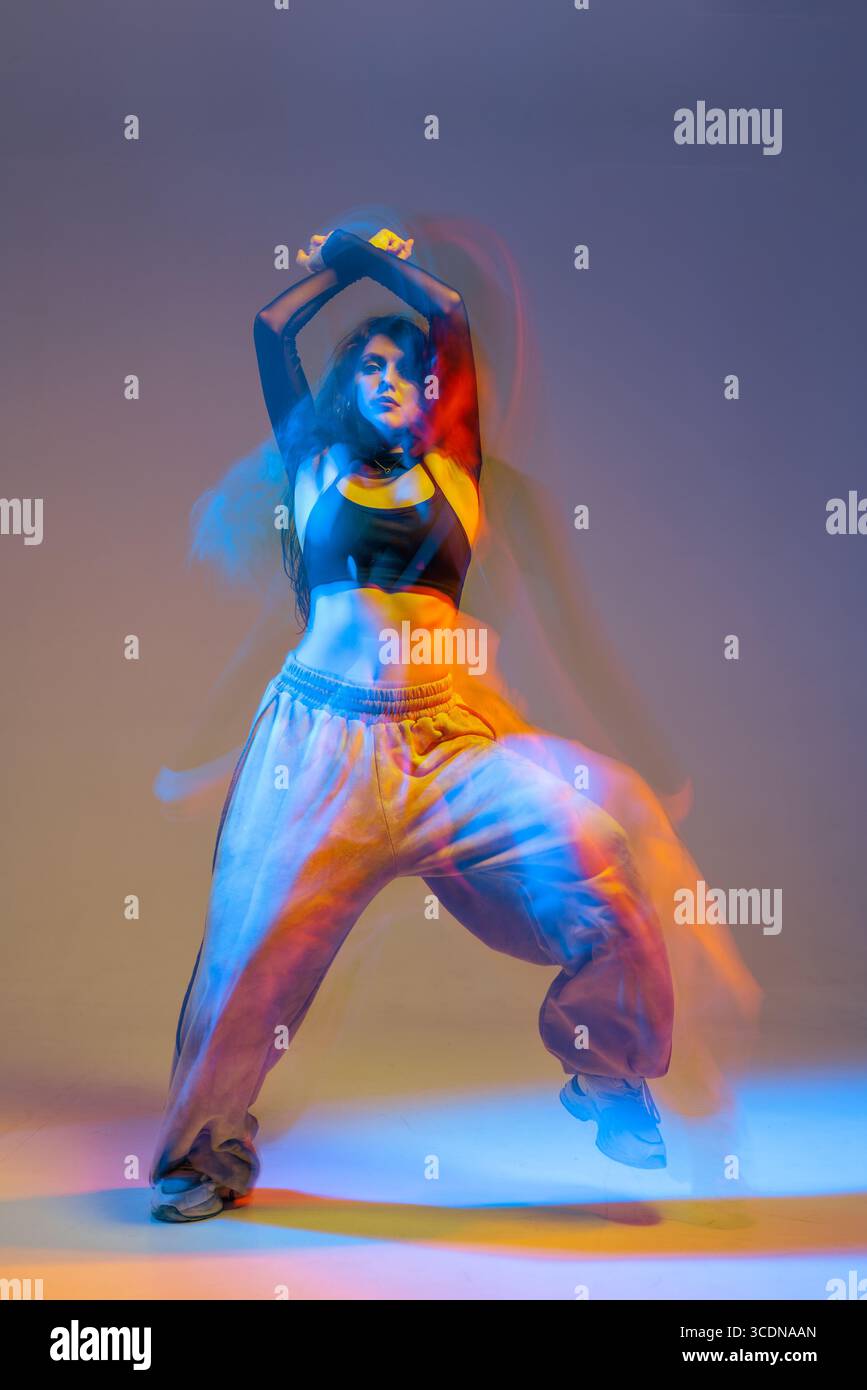 Energiegeladene Jazz-Funk-Tänzerin in moderner Sportbekleidung mit ausdrucksstarker Choreografie mit dynamischer Farbbeleuchtung. Stockfoto