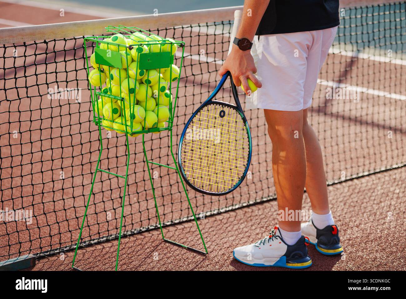 Nahaufnahme eines Tennistrainers mit Schläger und Basketballkorb auf dem Platz, bereit für den Unterricht oder das Training im Freien Stockfoto