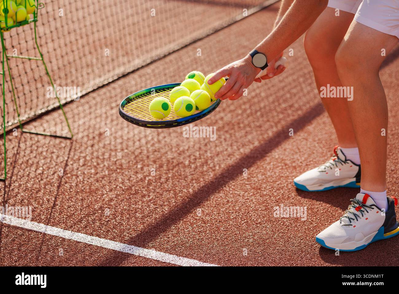 Nahaufnahme des Tennistrainers, der während des Trainings Bälle auf Schlägern sammelt, konzentrieren Sie sich auf Ausrüstung und Action auf dem Platz Stockfoto