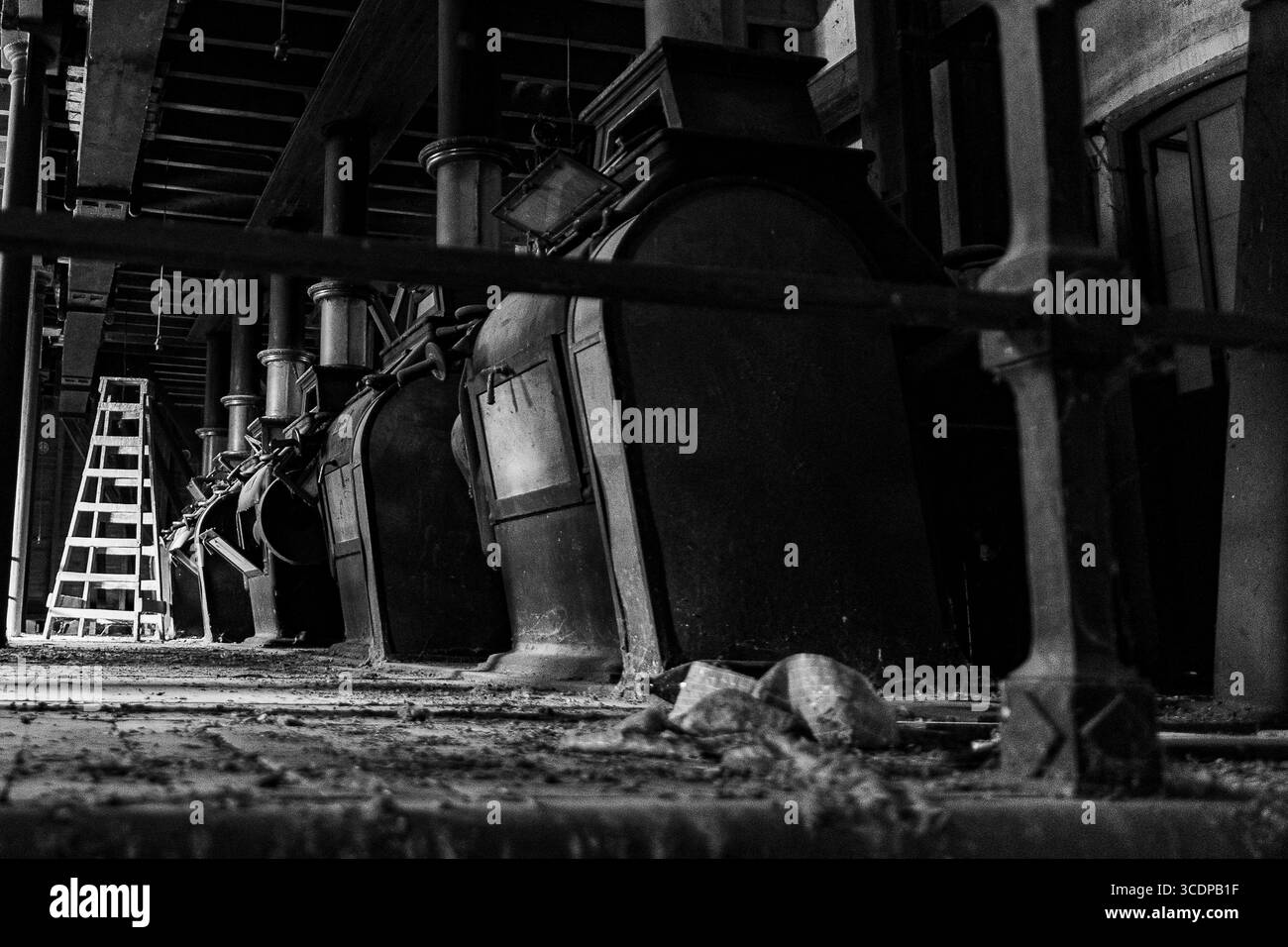 Alte Industriemaschinen in einer verlassenen Werkstatt mit rustikalen Holzbalken, die bei schwachem Licht zu sehen sind Stockfoto