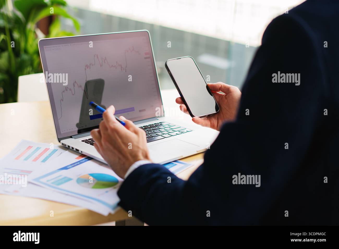 Unwiedererkennbarer eleganter junger Geschäftsmann in einem Anzug, der in einem Smartphone mit weißem Modell arbeitet, leerer Bildschirm und Laptop in einem Café in der Nähe Stockfoto