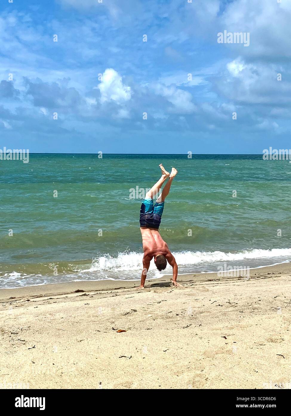 Junge Männer, die einen Handstand am Strand am Ufer des Karibischen Meeres machen. - Smartphone-aufgenommenes Stockfoto