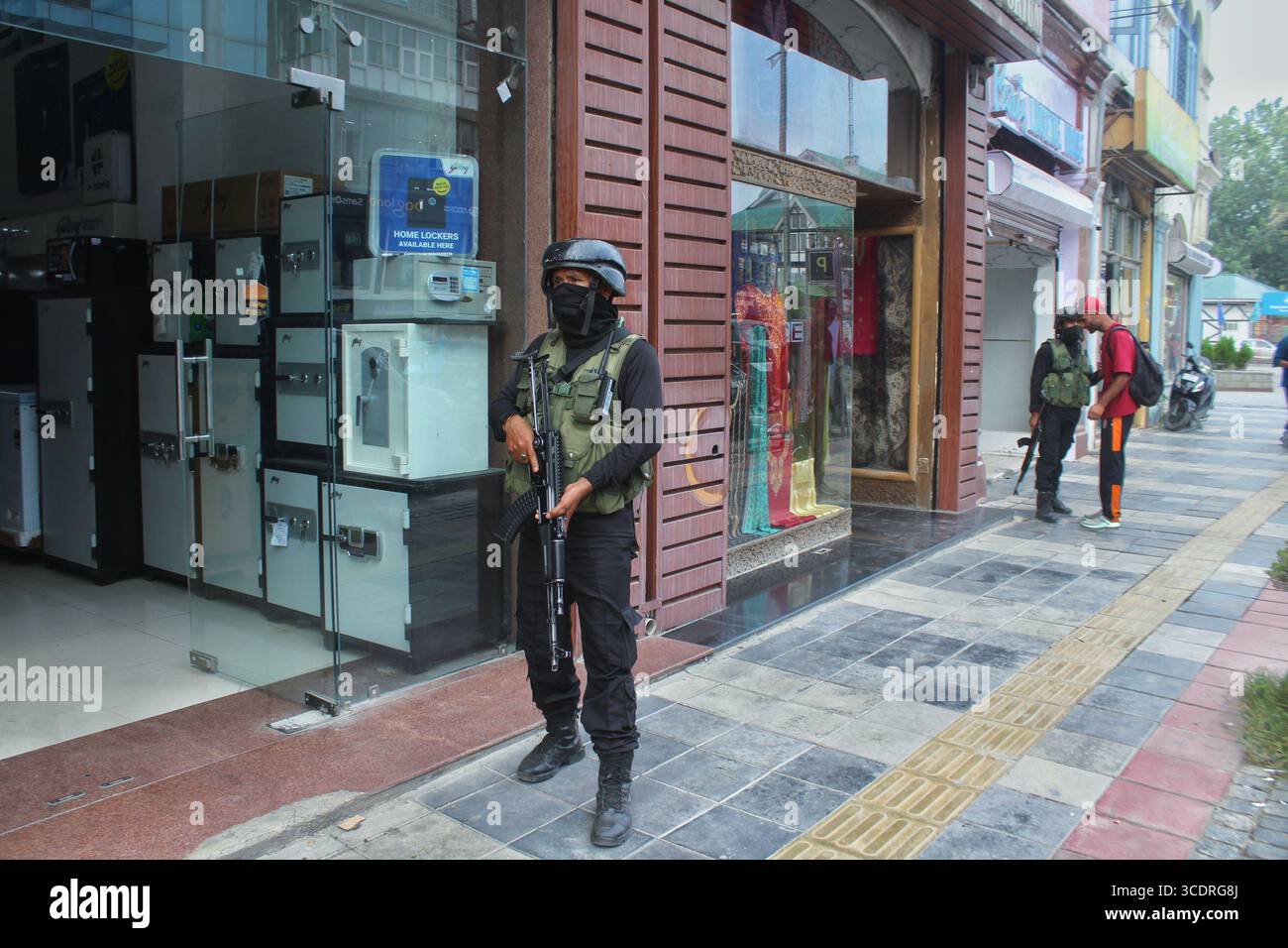Indische Sicherheitspersonal steht Wache, während ein anderer Fußgänger während des Frittierens in Srinagar am 14. August 2025 vor dem Unabhängigkeitstag 2025 frisst. Stockfoto