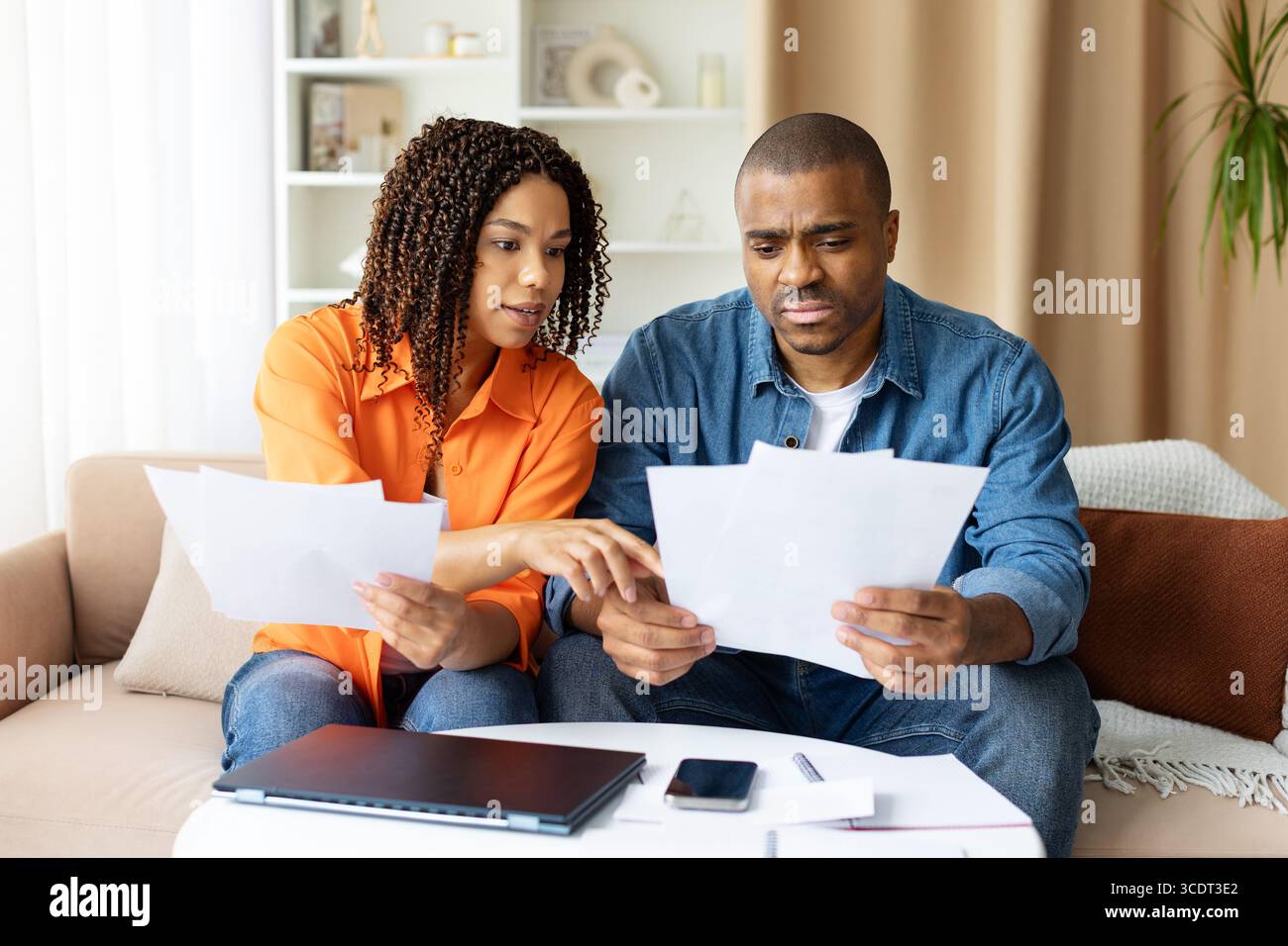 Ernsthaftes junges afroamerikanisches Paar, das Dokumente zu Hause zusammen überprüft Stockfoto