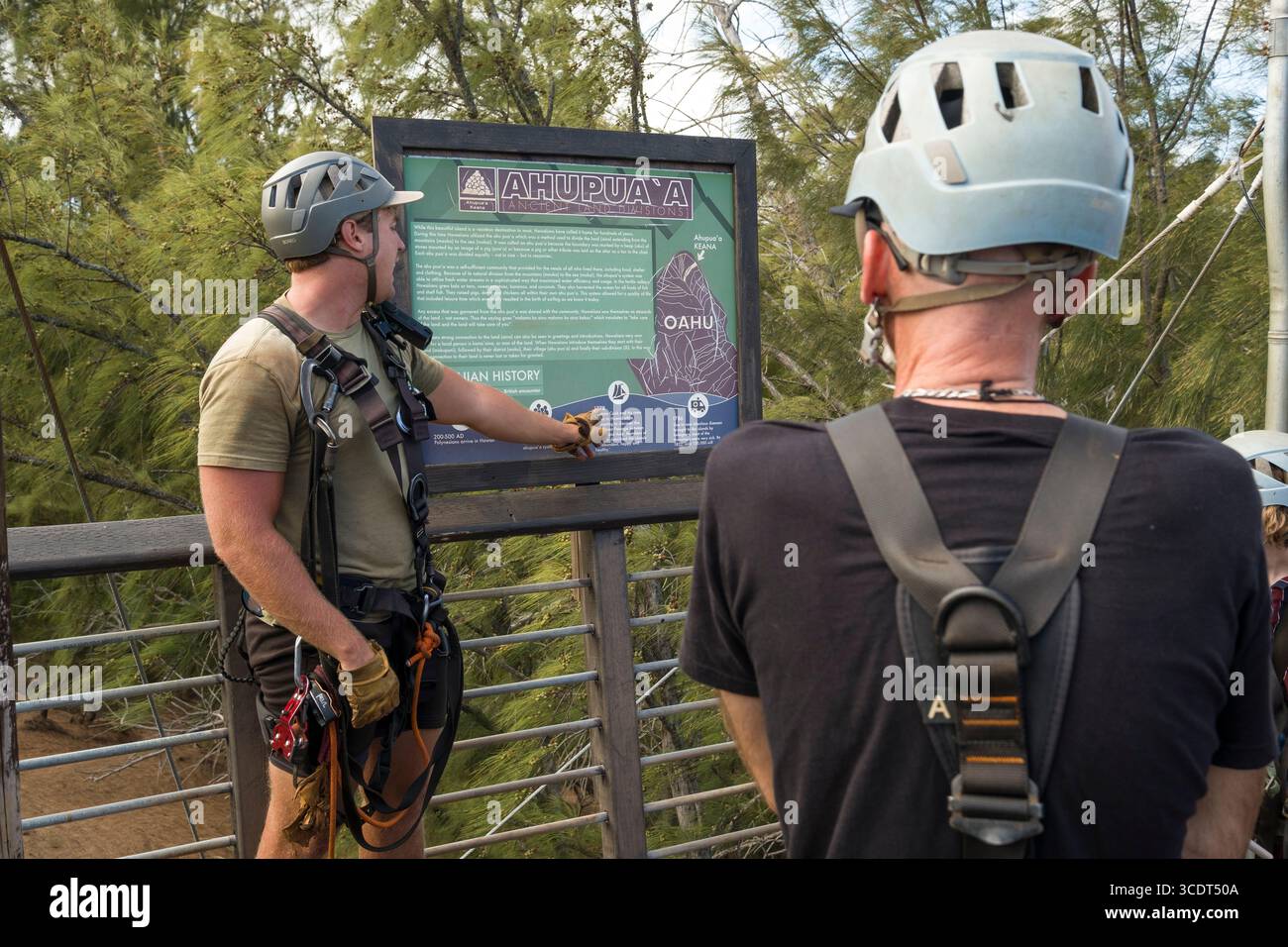 Männlicher Reiseleiter liest auf einem Schild über die hawaiianische Kultur der Gegend während einer geführten Seilrutsche an den CLIMB Works Keana Farms; Kahuku, Koolauloa, Honol Stockfoto