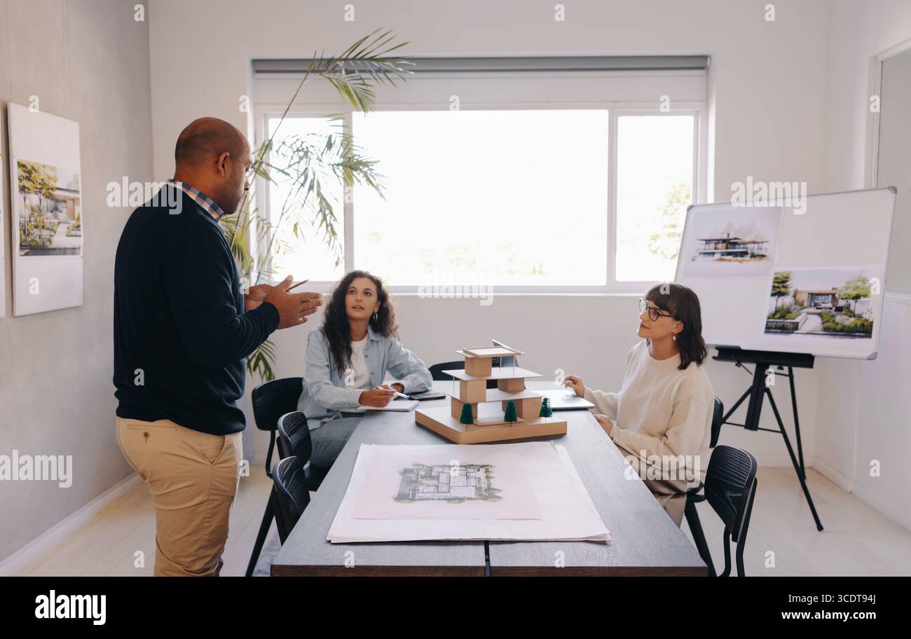 Eine Gruppe von Fachleuten, die Ideen an einem Tisch mit einem Projektmodell diskutieren, wobei der Schwerpunkt auf Teamarbeit und Kreativität in einer professionellen Büroumgebung liegt Stockfoto