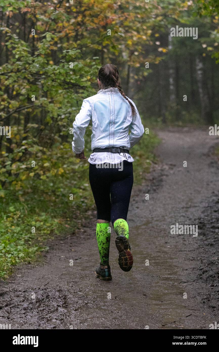 Weibliche Athletin, die beim Marathon bei starkem Regen einen schlammigen Waldweg läuft Stockfoto