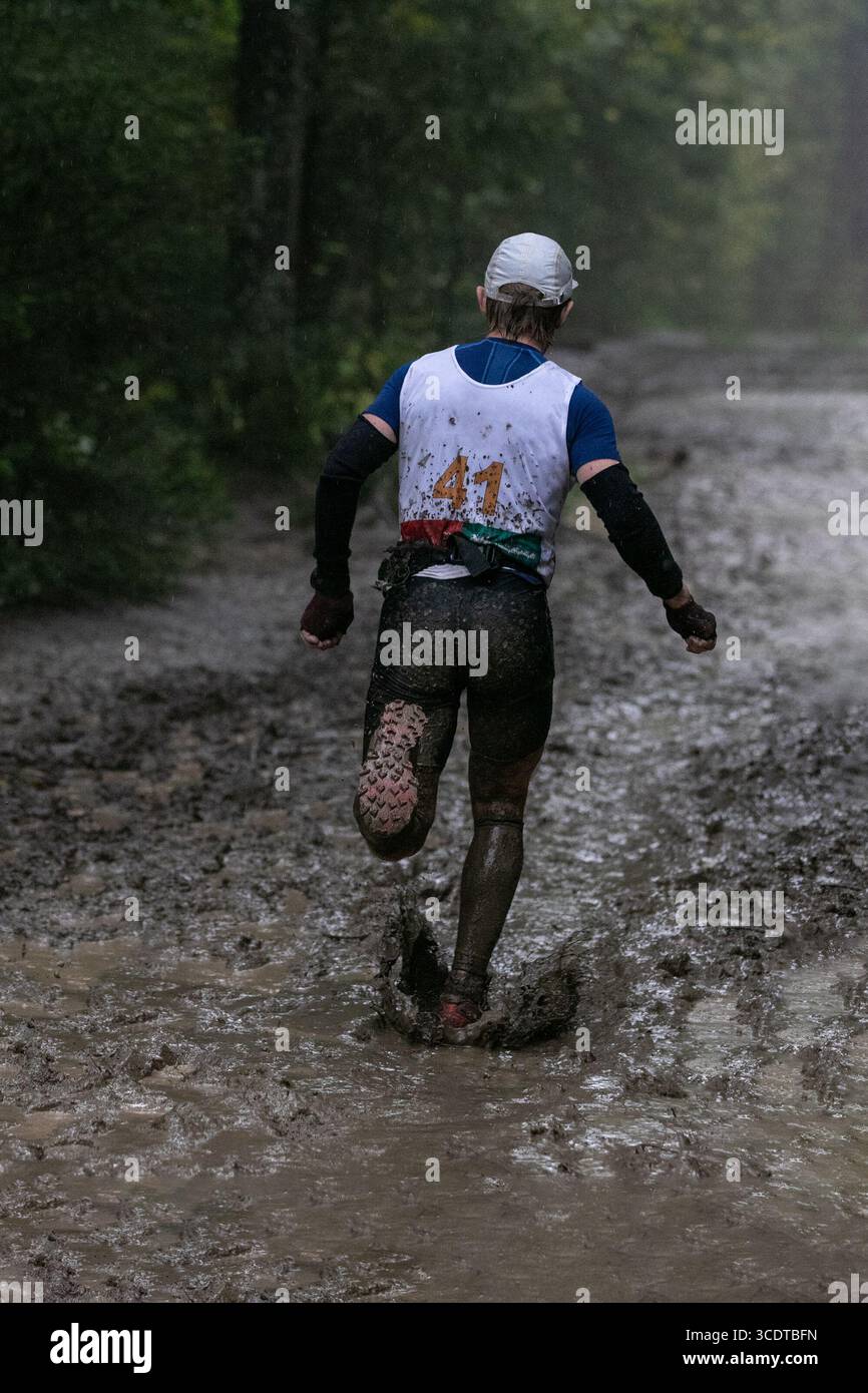 Sportler, die beim Marathon bei starkem Regen schlammige Waldwege laufen Stockfoto