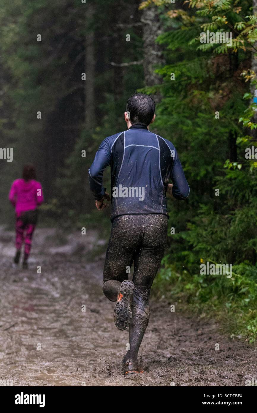 Athlet mit Rückansicht, der beim Marathon bei starkem Regen schlammige Waldpiste läuft Stockfoto