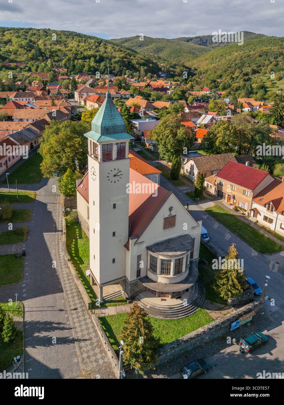 Aus der Vogelperspektive auf den markanten Kontrast zwischen den rot gekachelten Dächern und den grünen Hügeln rund um die Kirche, Pukanec, Region Nitra, Slowakei. Stockfoto