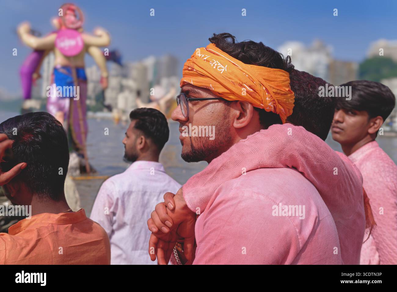 Während des Ganesh Chaturthi (Ganesh Festival) in Mumbai, Indien, umarmt ein junger Mann seinen Freund, eine große Ganesh-Statue im B/g, um in das Meer einzutauchen Stockfoto