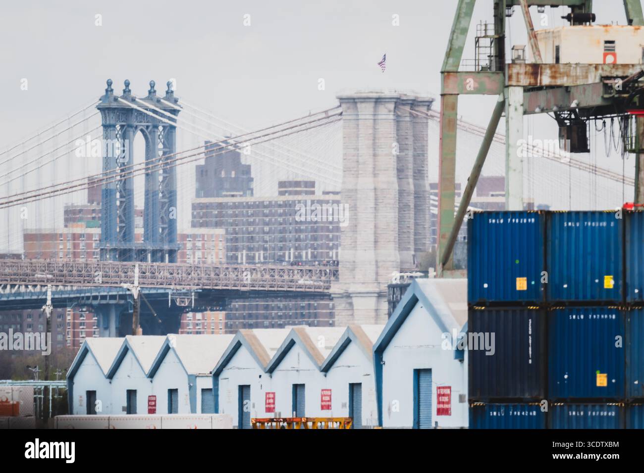 Der Blick auf die gestapelten blauen Versandcontainer steht in krassem Kontrast zu den zarten Brücken, die sich unter einem bewölkten Himmel befinden, in New York, New York, U Stockfoto