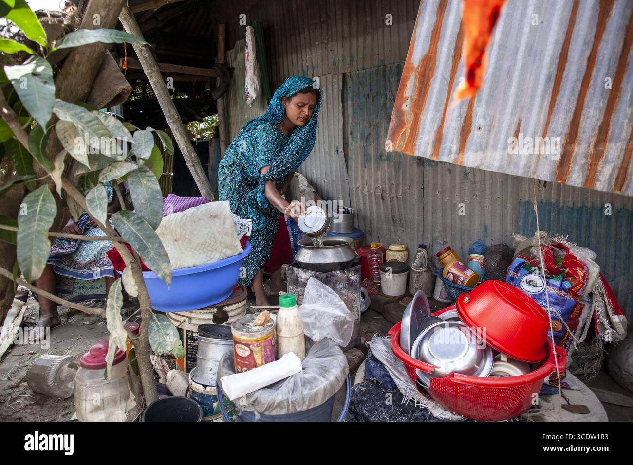 Feni, Bangladesch - 29. August 2024: Blick auf eine Frau in leuchtendem blaublauem Gewand inmitten einer bescheidenen Wohnung, die gewellten Eisenwände spiegeln ein einfaches Leben wider Stockfoto