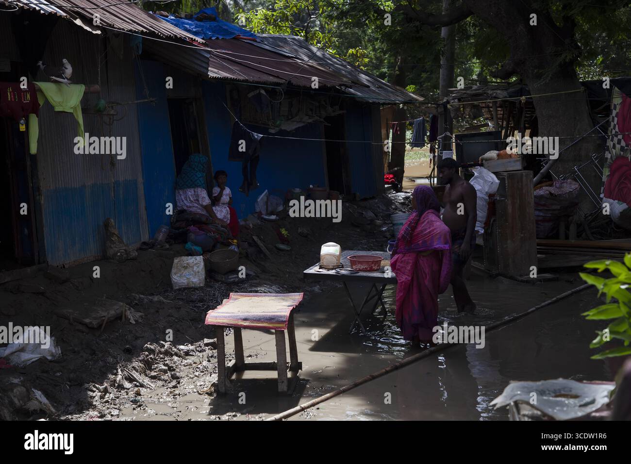Feni, Bangladesch - 29. August 2024: Blick auf das Hochwasser, das die Wellblechdächer bescheidener Wohnungen reflektiert, während die Menschen durch die untergetauchte Landschaft navigieren. Stockfoto