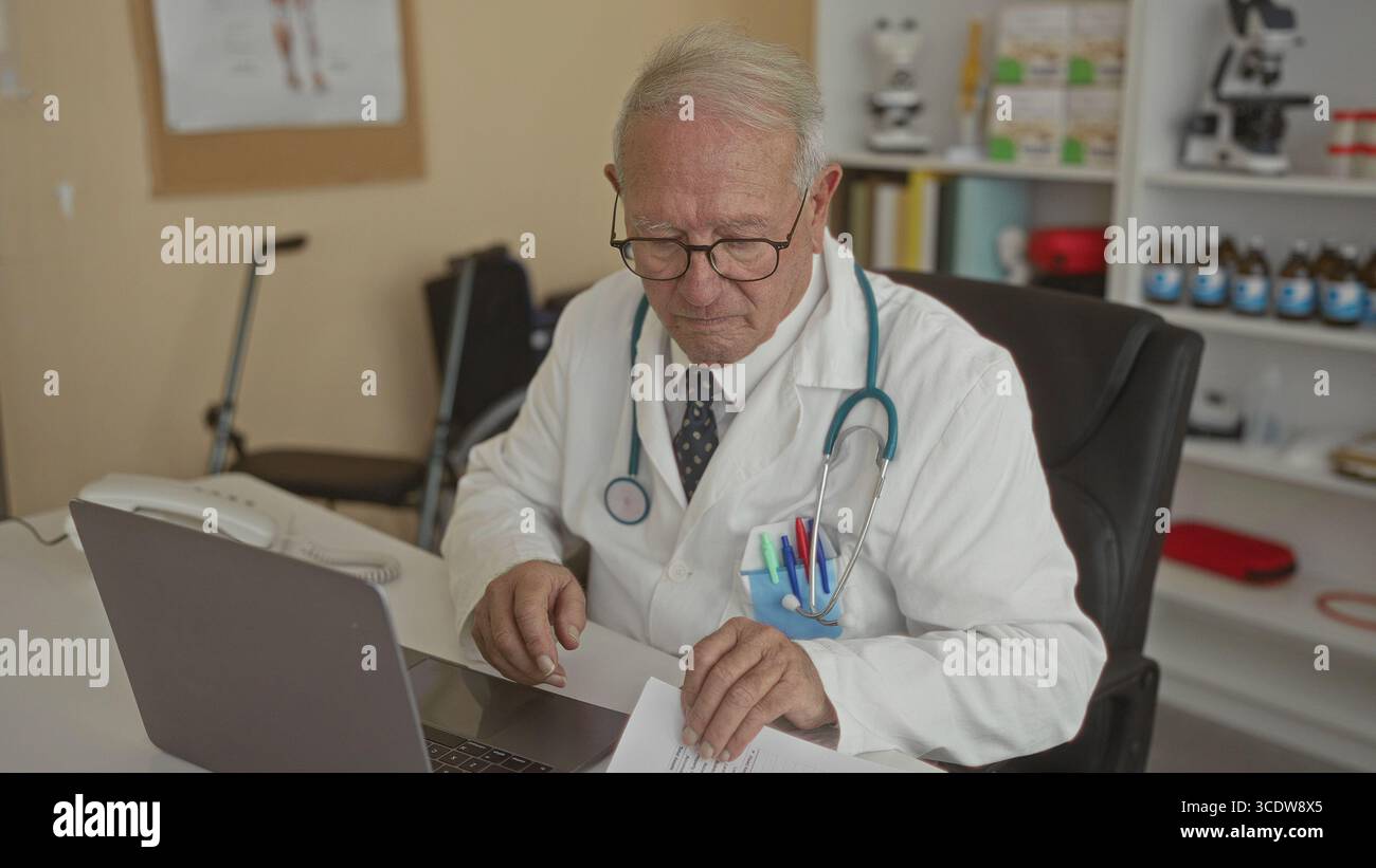 Senior Mann in einer Arztuniform arbeitet drinnen in einer Klinik, untersucht Dokumente mit einem Stethoskop sichtbar, repräsentiert eine professionelle Gesundheitsfürsorge e Stockfoto