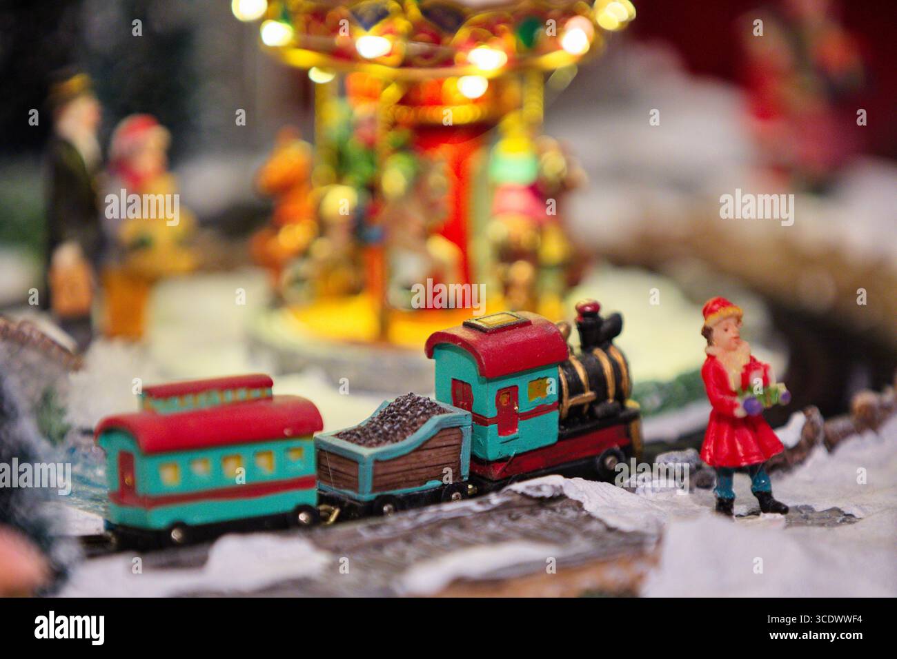 Miniatur-Feriendorf mit Spielzeugzug, Karussellbeleuchtung und Figuren auf verschneiten Böden, ein Studio-Stillleben für kommerzielle und redaktionelle Lizenzierung. Stockfoto