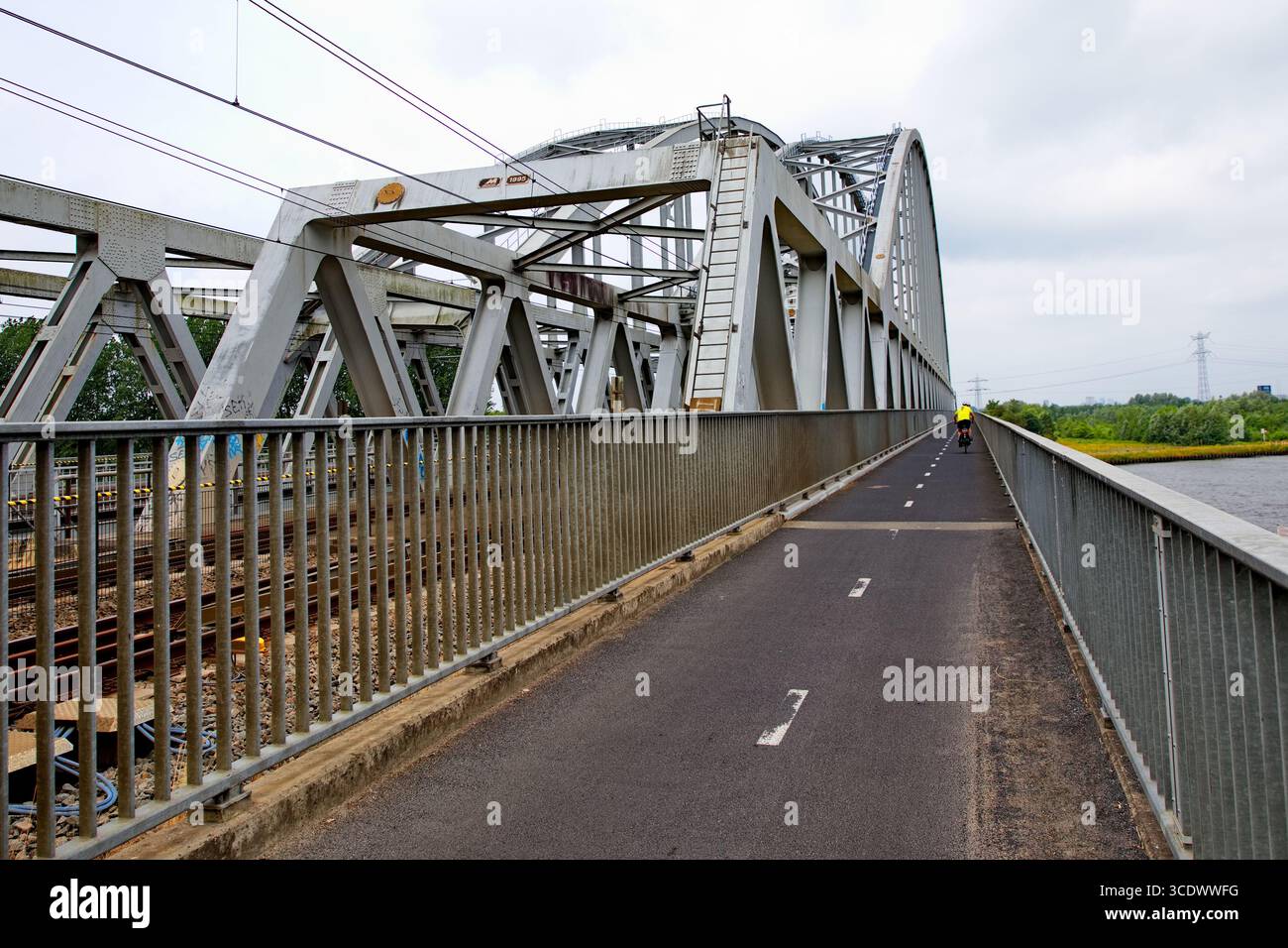 Stahlfachwerkbahnbrücke mit Radweg über einen Fluss in den Niederlanden, verschwindende Strecken und Einzelradfahrer bilden eine Reise- und Redaktionsszene. Stockfoto