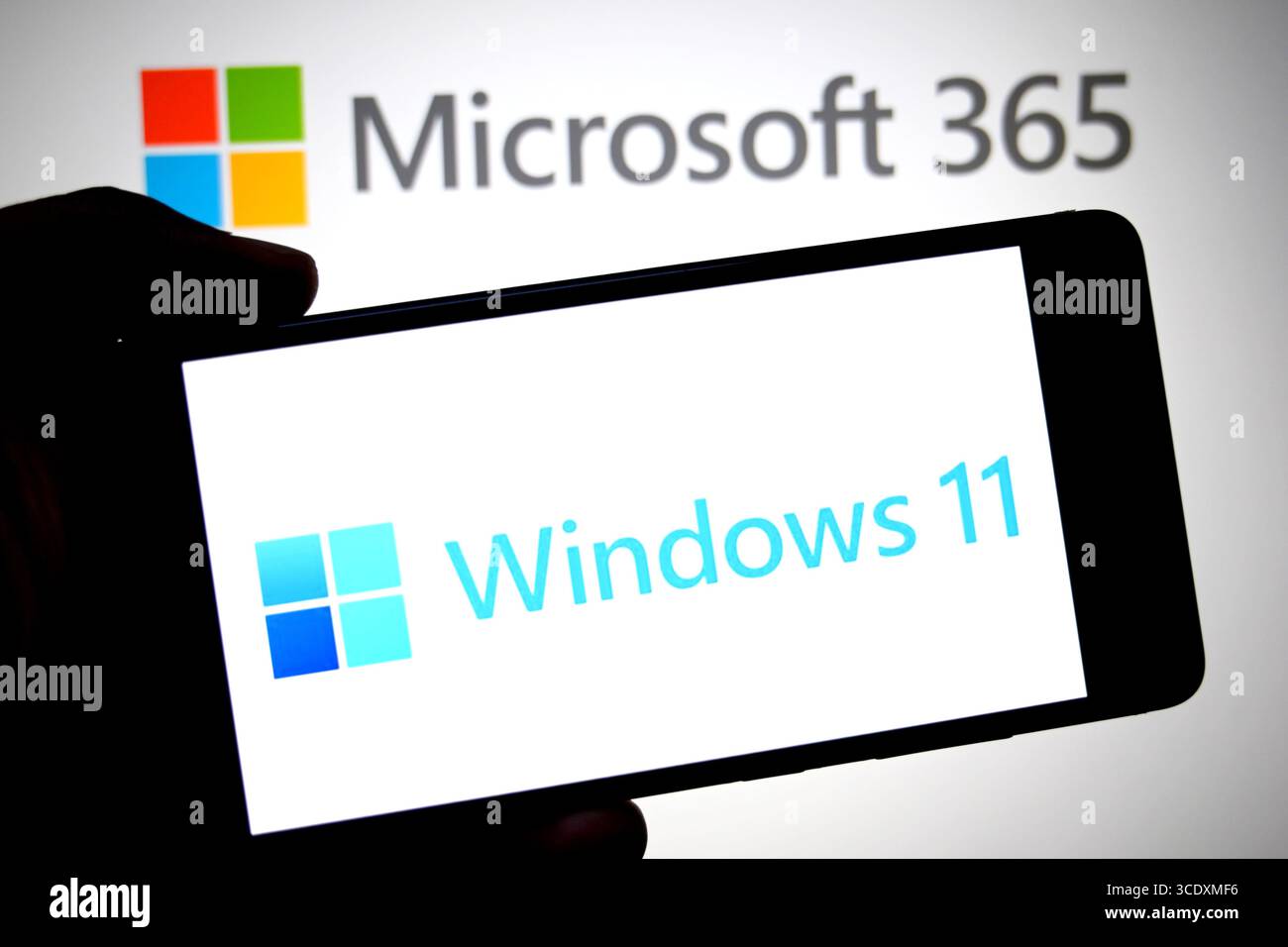 In dieser Abbildung wird ein Windows 11-Logo auf einem Smartphone mit einem Microsoft 365-Logo im Hintergrund angezeigt. Stockfoto