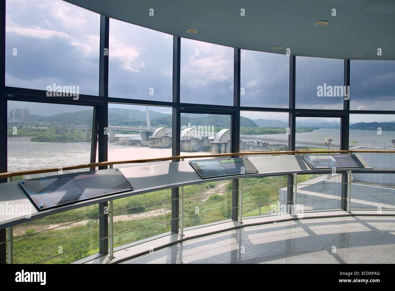Von einer geschwungenen Beobachtungsgalerie aus umrahmen Fenster das Gangjeong Goryeong Weir am Nakdong River in Daegu, mit Interpretationstafeln entlang der Schiene und Stockfoto