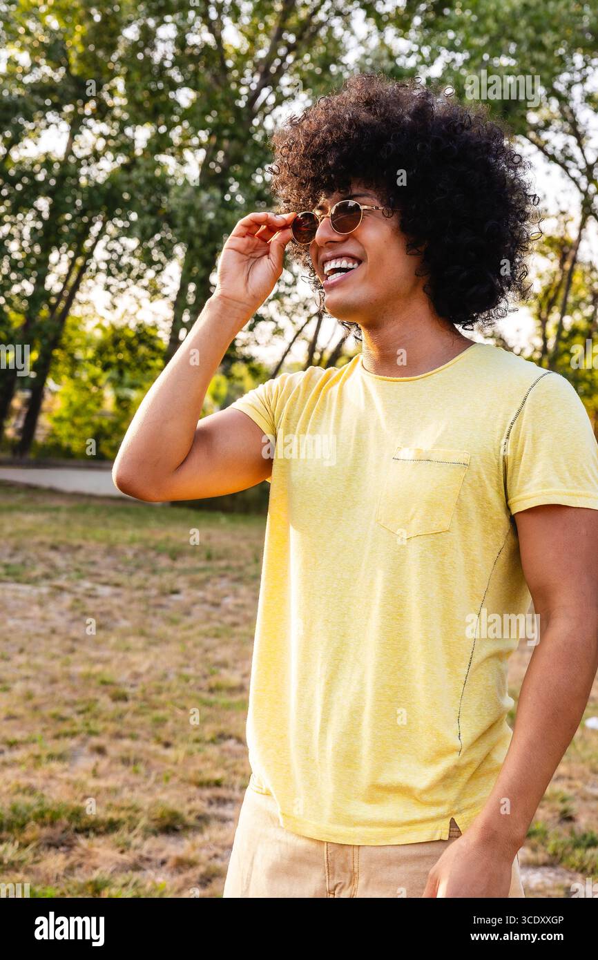 Ein junger Mann mit Sonnenbrille und einem Lächeln im Park Stockfoto