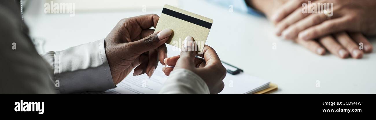 Kopfzeile der schwarzen Frau, die Kreditkarte hält, während sie mit einem männlichen Angestellten im Bankbüro über finanzielle Angelegenheiten sprach, beide sitzen am Schreibtisch mit sichtbaren Dokumenten, Händen und Karte im Fokus Stockfoto