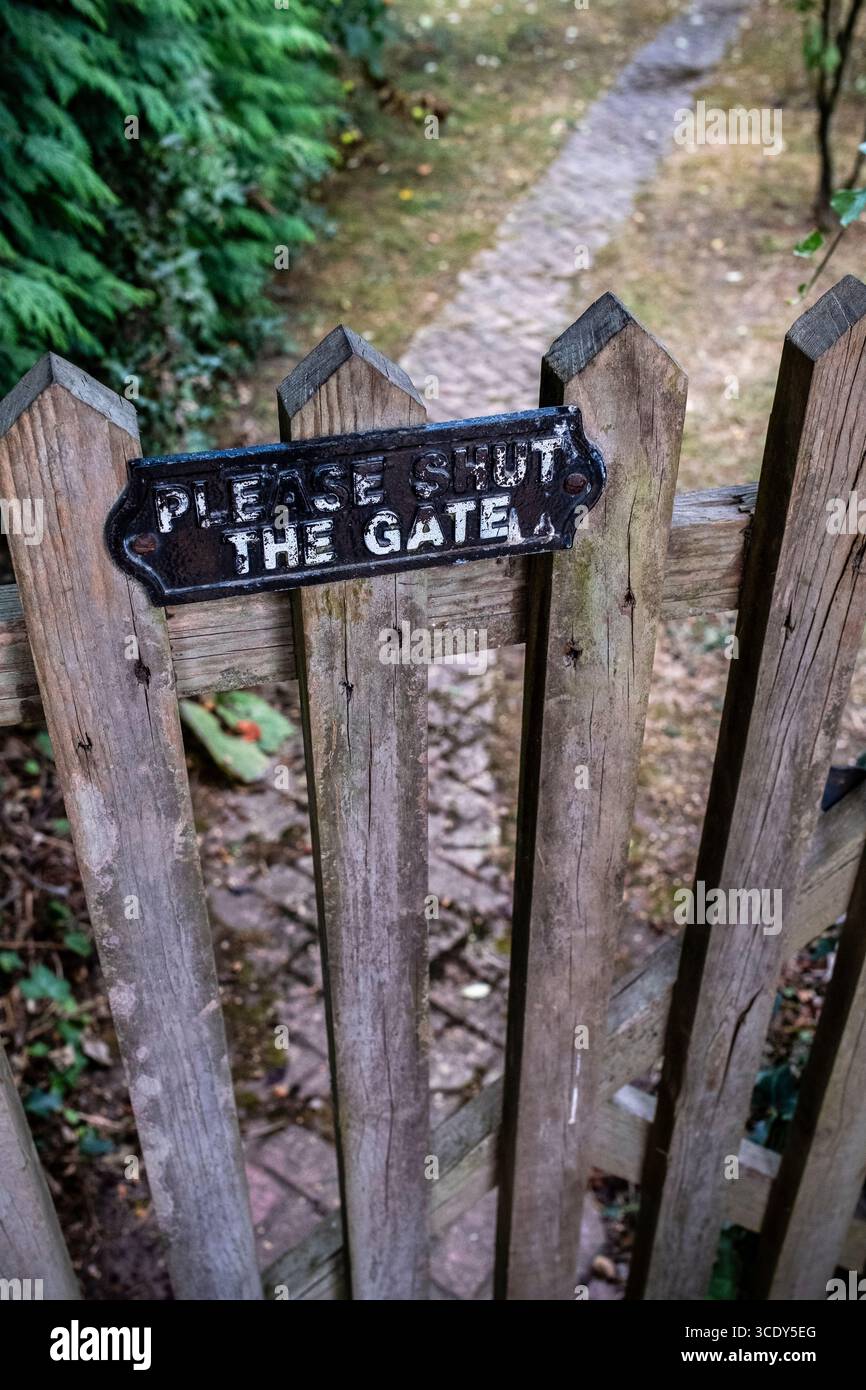 Hölzernes Gartentor mit Schild, etwas altes unbekümmertes Schild am Tor, Weg und Garten im Hintergrund Stockfoto