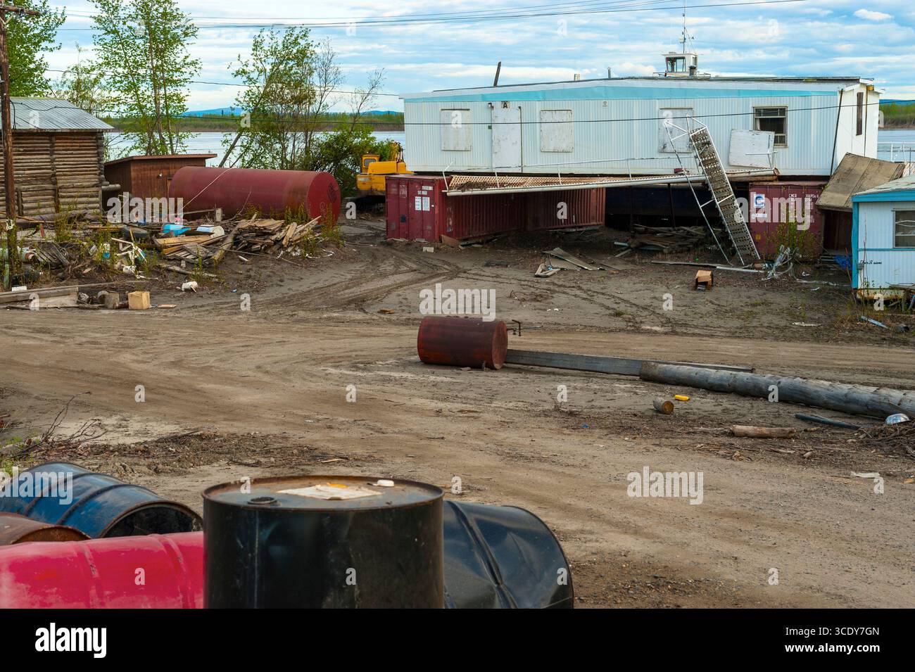 Ein Nebenhof mit einem zertrümmerten Gebäude, das auf Versandcontainern, 55-Gallonen-Fässern und Trödel in Galena, Alaska, USA, gestapelt ist Stockfoto