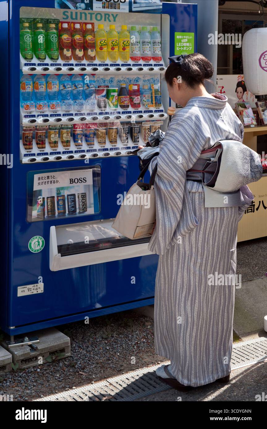 Frau, die einen traditionellen japanischen Kimono trägt, kauft ein Getränk aus einem modernen Getränkeautomaten für einen Kontrast von Neu und Alt in Kyoto, Japan. Stockfoto