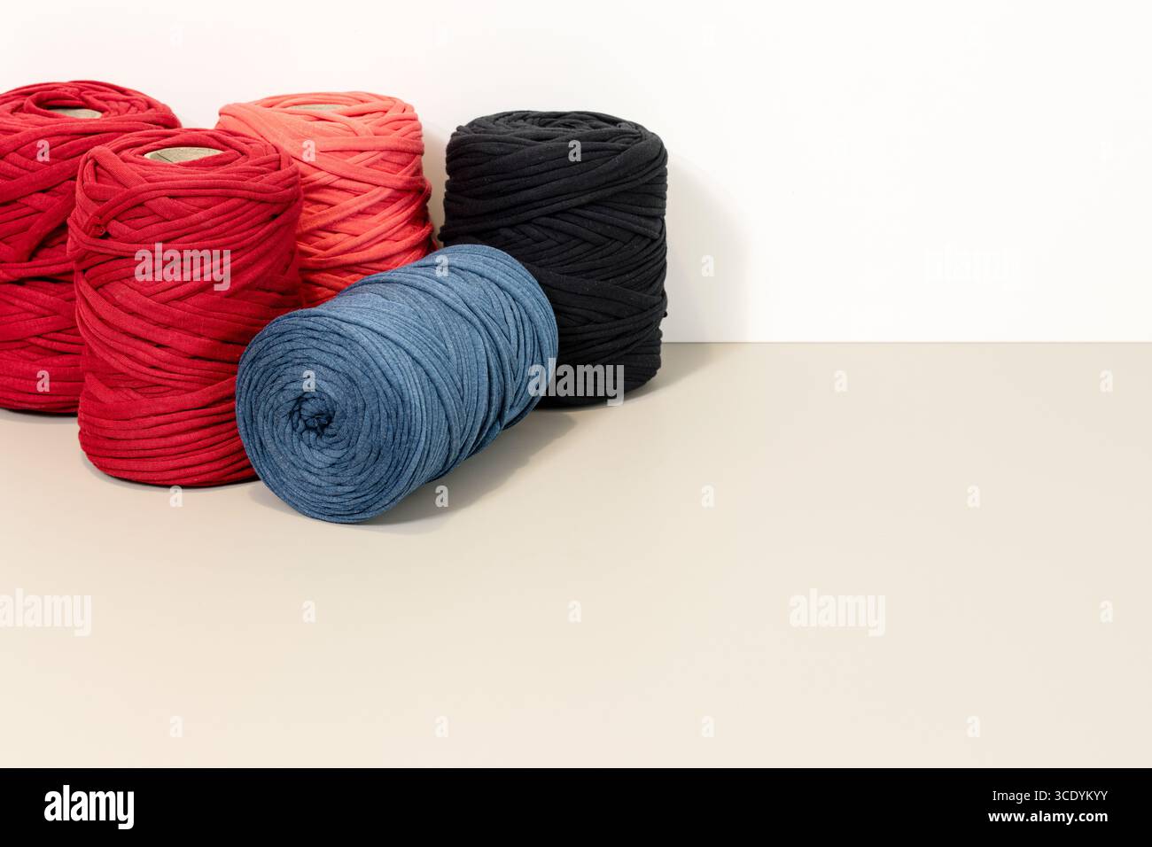 Hintergrund einer Gruppe von Spulen aus recyceltem T-Shirt-Garn, die auf einem beigefarbenen Tisch vor einer weißen Wand angeordnet sind. Kopierbereich Stockfoto