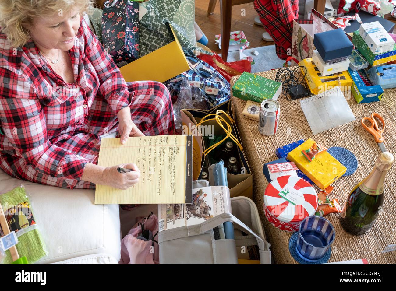 Frau, die auf gelbem Pad schreibt, um die Geschenke zu verfolgen, die am Weihnachtsmorgen in den USA eingegangen sind Stockfoto