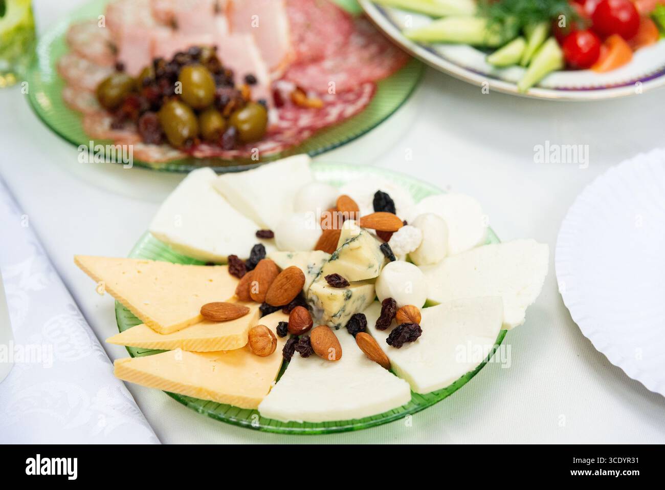 Eine appetitliche Käseplatte mit verschiedenen Käsesorten, Nüssen und Oliven, perfekt für Treffen. Teller mit frischem Gemüse und Aufschnitt Stockfoto