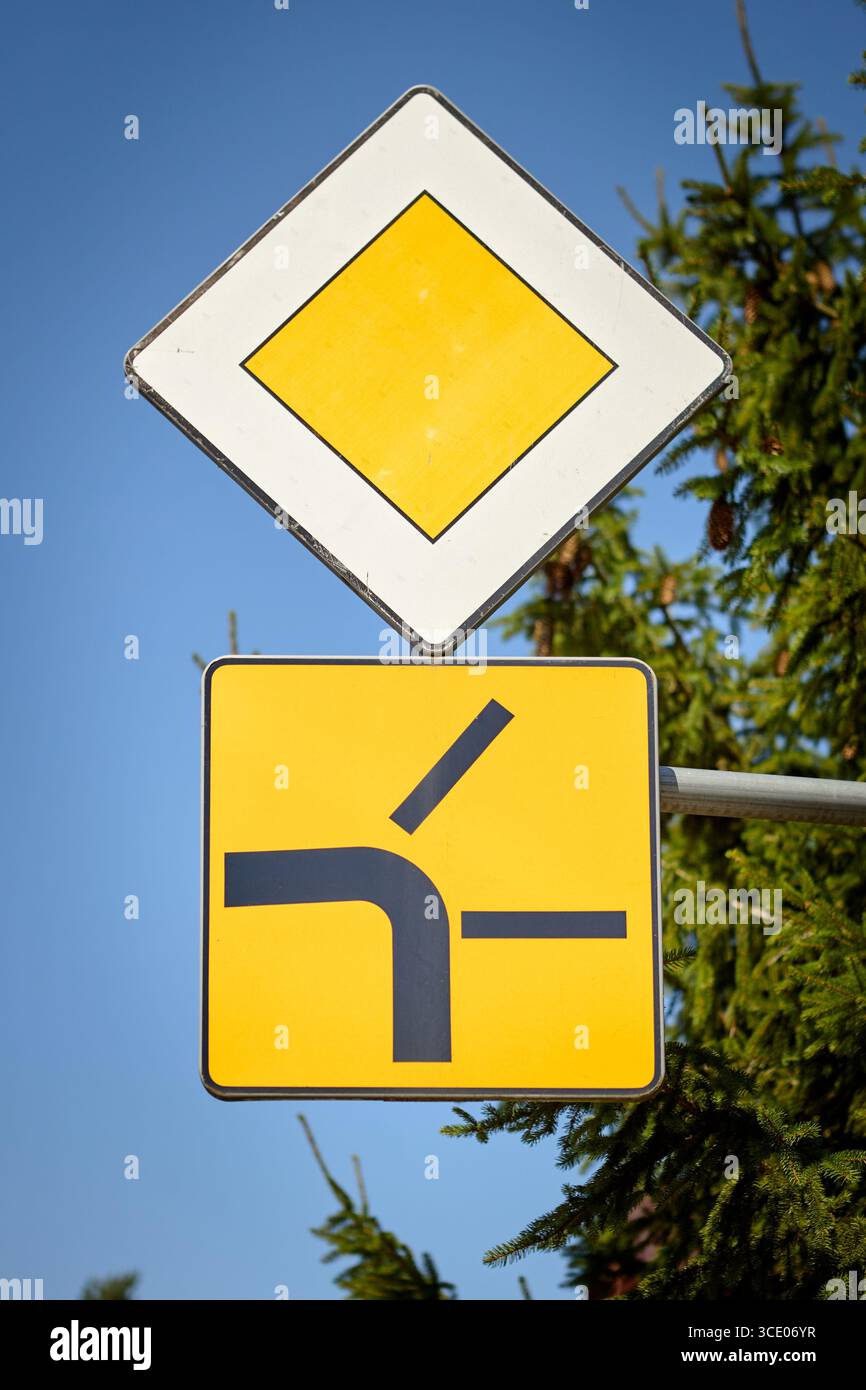 Kombination aus Straßenschildern mit einem gelben Diamanten, der die vorrangige Straße anzeigt, und einem zusätzlichen Schild, das eine Seitenstraße zeigt, die von links zusammenführt. Verwendet für einen Stockfoto