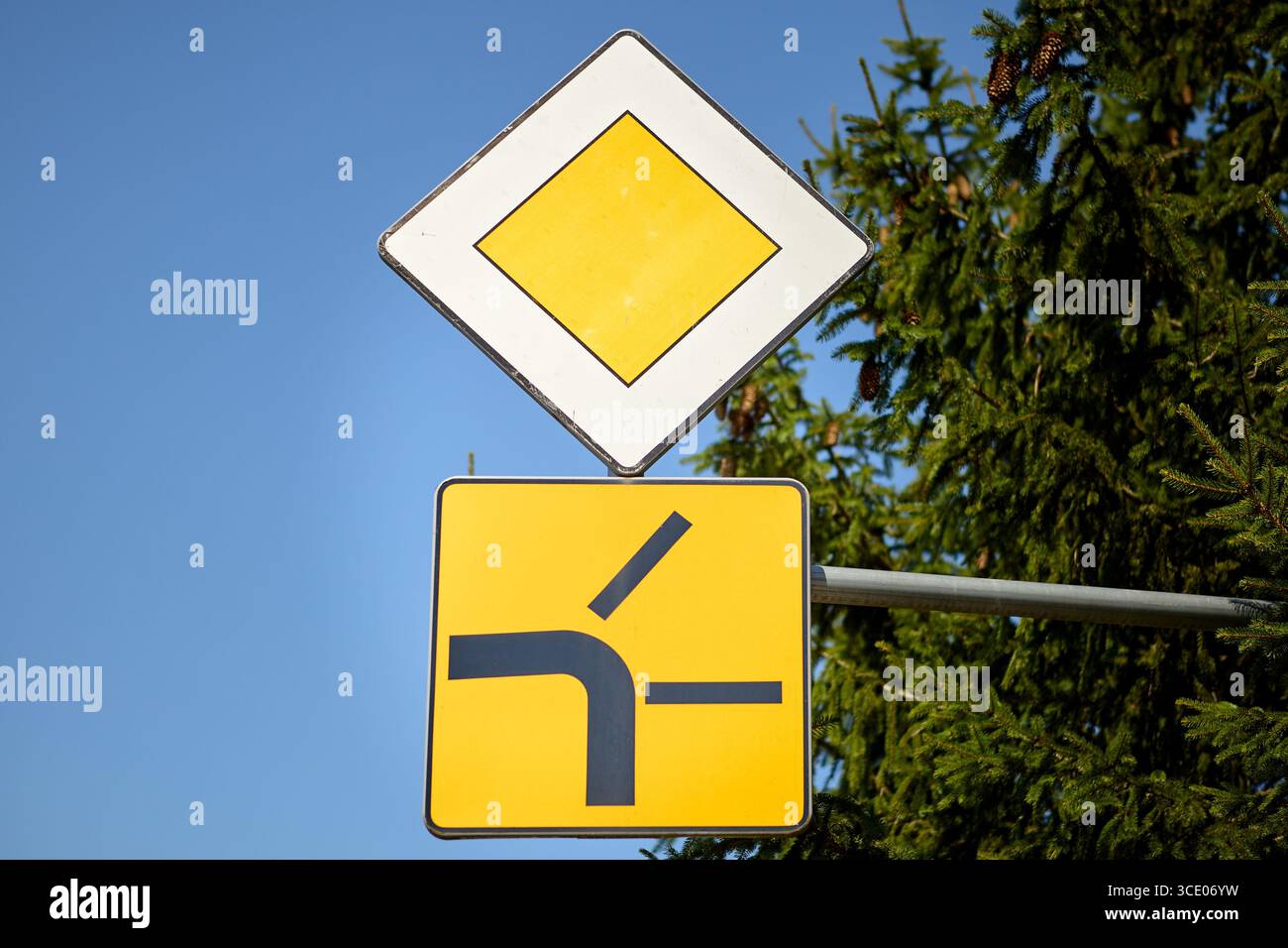 Kombination aus Straßenschildern mit einem gelben Diamanten, der die vorrangige Straße anzeigt, und einem zusätzlichen Schild, das eine Seitenstraße zeigt, die von links zusammenführt. Verwendet für einen Stockfoto