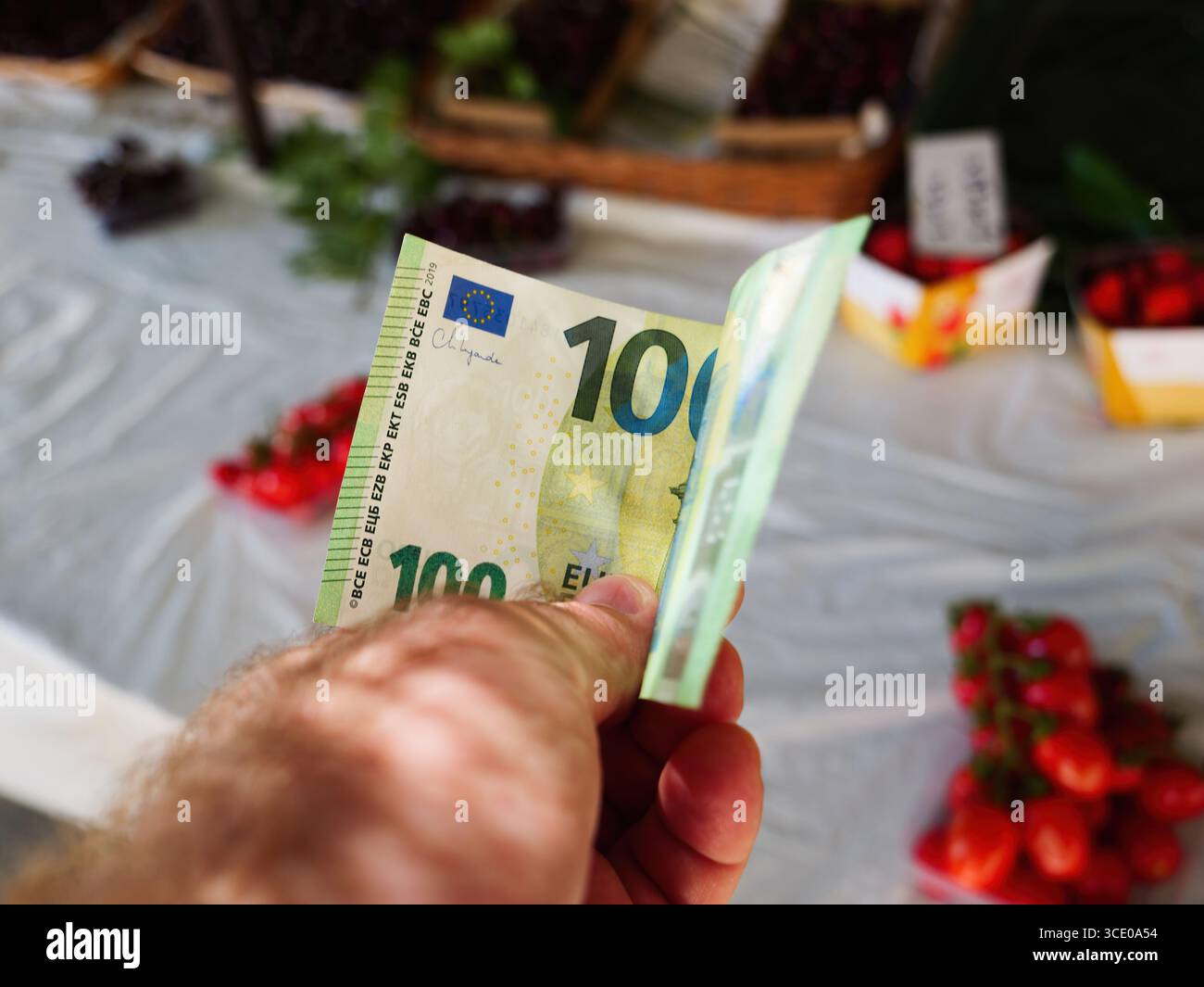 Nahaufnahme einer Hand mit einer 100-Euro-Banknote an einem Marktstand im Freien auf Mallorca mit verschwommenem Hintergrund frischer Produkte Stockfoto