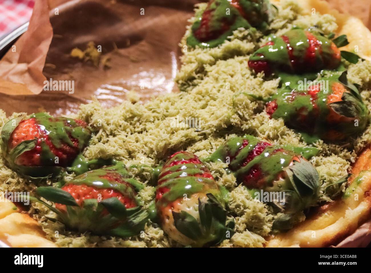 Erdbeerkuchen-Dessert mit cremigem Matcha und geriebenem grünem Teekäse, eine farbenfrohe thailändische Delikatesse auf einem lebhaften Nachtmarkt. Stockfoto