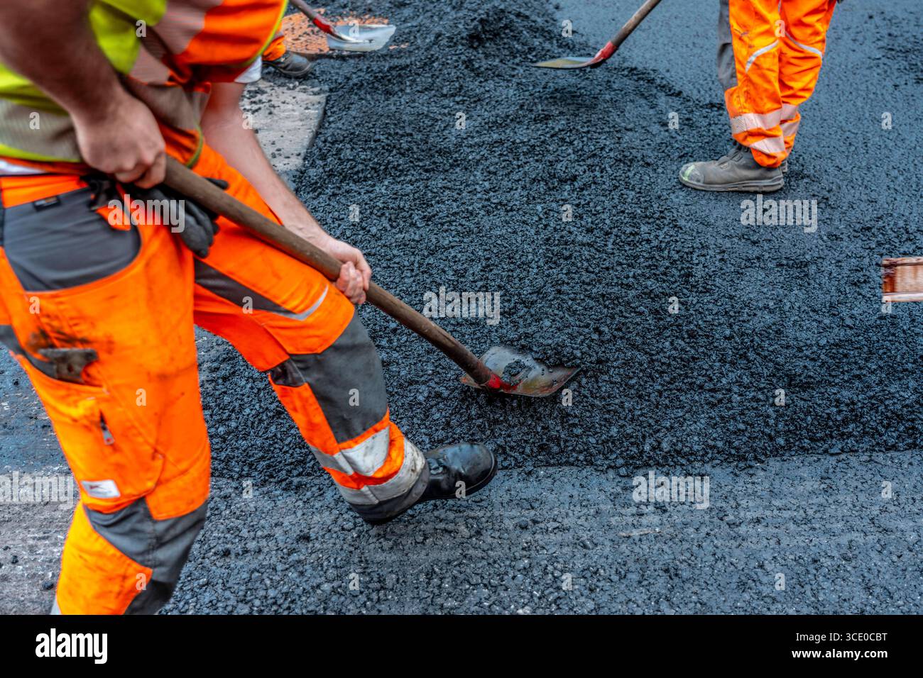 Straßenbau, Straßenbauarbeiten, Arbeiter bessern einen Teil einer innerstädtischen Straße mit Asphalt aus, der heiße Asphalt wird von Hand um einen Kanaldeckel verteilt, anschließend mit einer Straßenwalze verdichtet und geplättet, NRW, Deutschland, Straßenbau *** Straßenbau, Straßenbauarbeiten, Arbeiter reparieren einen Teil einer innerstädtischen Straße mit Asphalt, der heisse Asphalt wird von Hand um einen Mannlochdeckel verteilt, dann mit einer Straßenwalze verdichten und abflacht, NRW, Deutschland, Straßenbau, Straßenbau Stockfoto