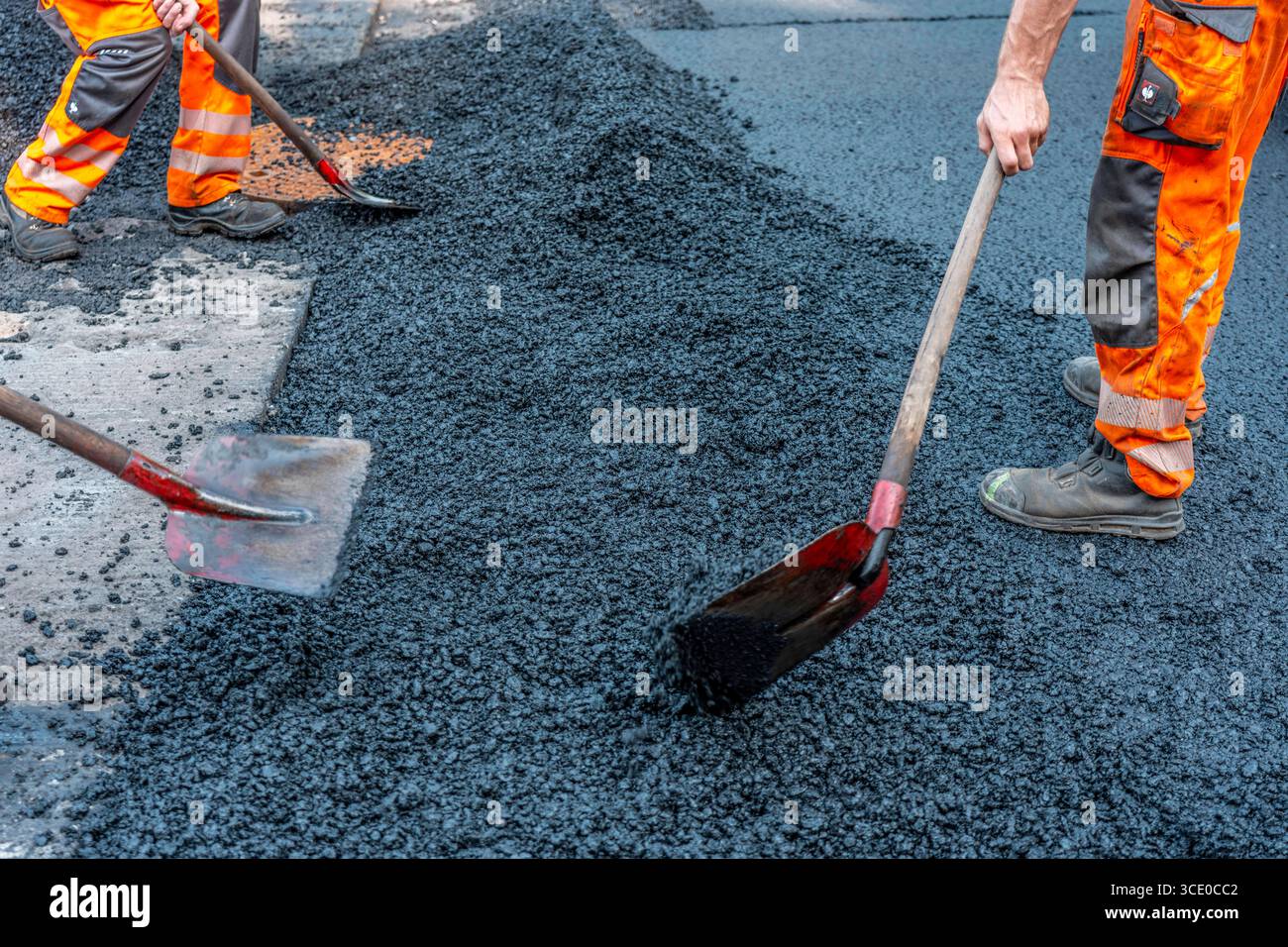 Straßenbau, Straßenbauarbeiten, Arbeiter bessern einen Teil einer innerstädtischen Straße mit Asphalt aus, der heiße Asphalt wird von Hand um einen Kanaldeckel verteilt, anschließend mit einer Straßenwalze verdichtet und geplättet, NRW, Deutschland, Straßenbau *** Straßenbau, Straßenbauarbeiten, Arbeiter reparieren einen Teil einer innerstädtischen Straße mit Asphalt, der heisse Asphalt wird von Hand um einen Mannlochdeckel verteilt, dann mit einer Straßenwalze verdichten und abflacht, NRW, Deutschland, Straßenbau, Straßenbau Stockfoto