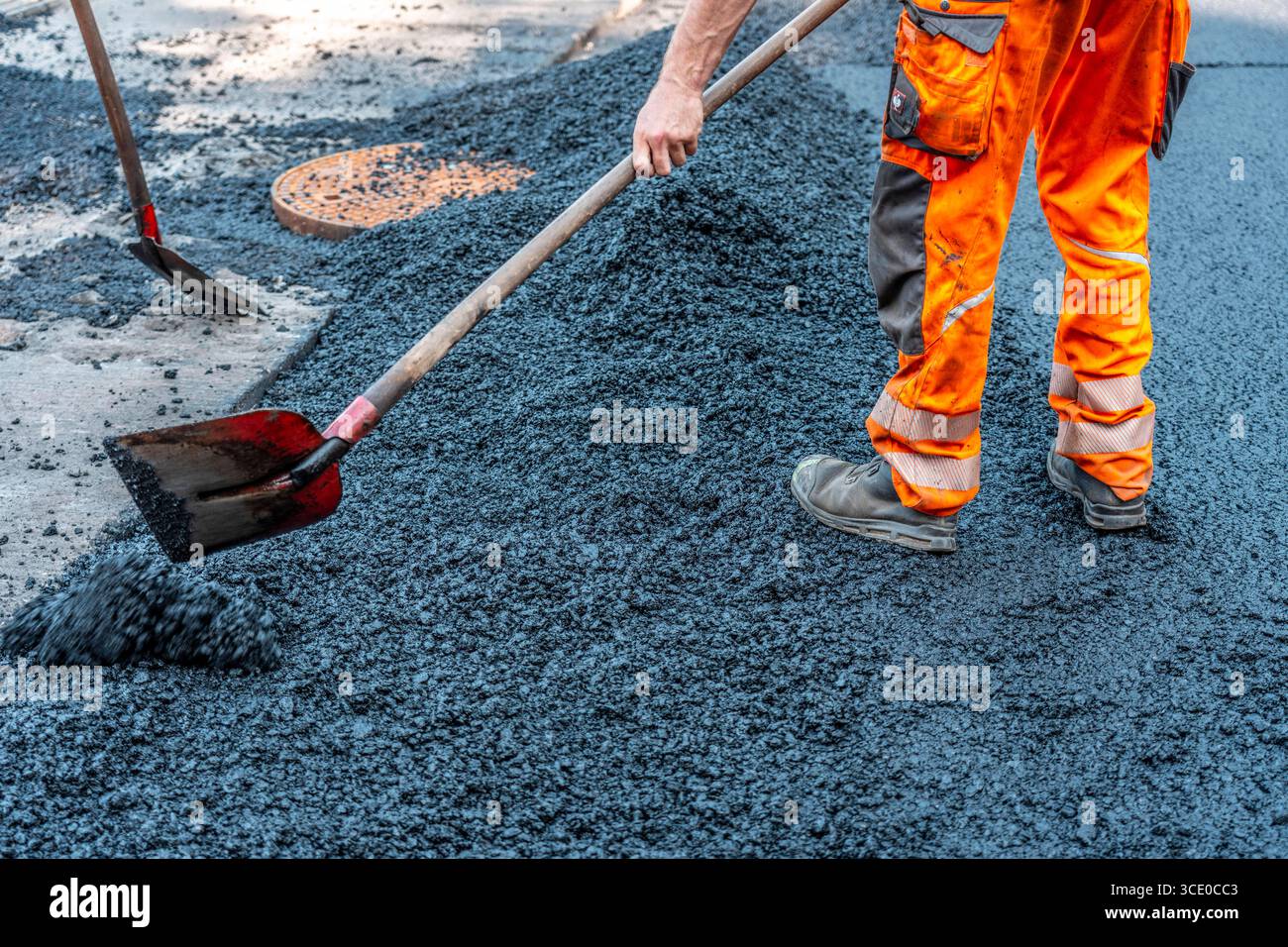 Straßenbau, Straßenbauarbeiten, Arbeiter bessern einen Teil einer innerstädtischen Straße mit Asphalt aus, der heiße Asphalt wird von Hand um einen Kanaldeckel verteilt, anschließend mit einer Straßenwalze verdichtet und geplättet, NRW, Deutschland, Straßenbau *** Straßenbau, Straßenbauarbeiten, Arbeiter reparieren einen Teil einer innerstädtischen Straße mit Asphalt, der heisse Asphalt wird von Hand um einen Mannlochdeckel verteilt, dann mit einer Straßenwalze verdichten und abflacht, NRW, Deutschland, Straßenbau, Straßenbau Stockfoto