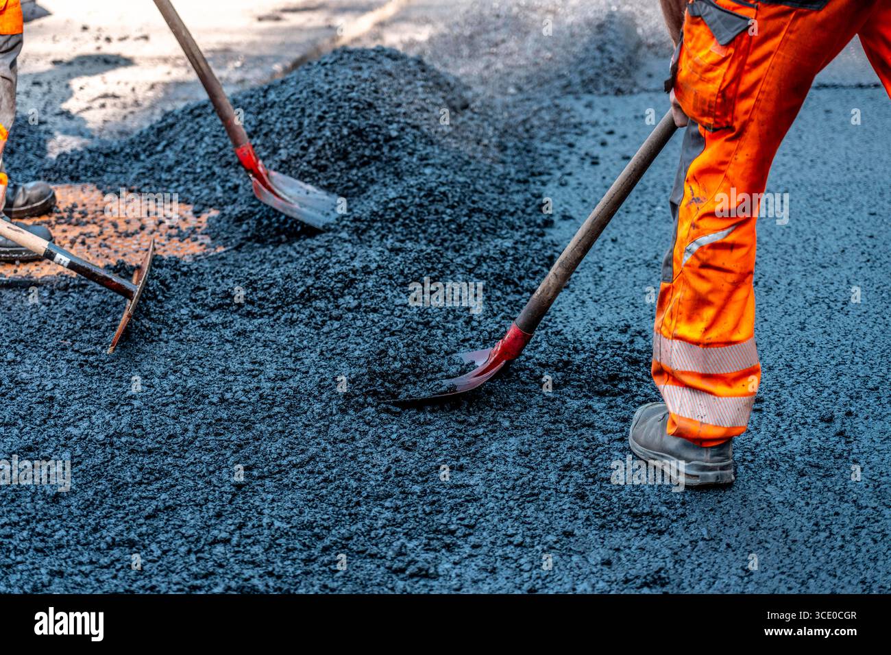 Straßenbau, Straßenbauarbeiten, Arbeiter bessern einen Teil einer innerstädtischen Straße mit Asphalt aus, der heiße Asphalt wird von Hand um einen Kanaldeckel verteilt, anschließend mit einer Straßenwalze verdichtet und geplättet, NRW, Deutschland, Straßenbau *** Straßenbau, Straßenbauarbeiten, Arbeiter reparieren einen Teil einer innerstädtischen Straße mit Asphalt, der heisse Asphalt wird von Hand um einen Mannlochdeckel verteilt, dann mit einer Straßenwalze verdichten und abflacht, NRW, Deutschland, Straßenbau, Straßenbau Stockfoto