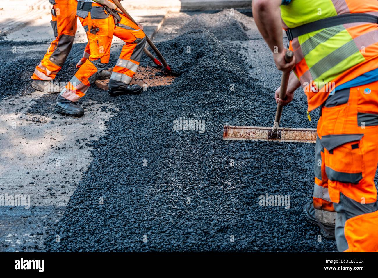 Straßenbau, Straßenbauarbeiten, Arbeiter bessern einen Teil einer innerstädtischen Straße mit Asphalt aus, der heiße Asphalt wird von Hand um einen Kanaldeckel verteilt, anschließend mit einer Straßenwalze verdichtet und geplättet, NRW, Deutschland, Straßenbau *** Straßenbau, Straßenbauarbeiten, Arbeiter reparieren einen Teil einer innerstädtischen Straße mit Asphalt, der heisse Asphalt wird von Hand um einen Mannlochdeckel verteilt, dann mit einer Straßenwalze verdichten und abflacht, NRW, Deutschland, Straßenbau, Straßenbau Stockfoto