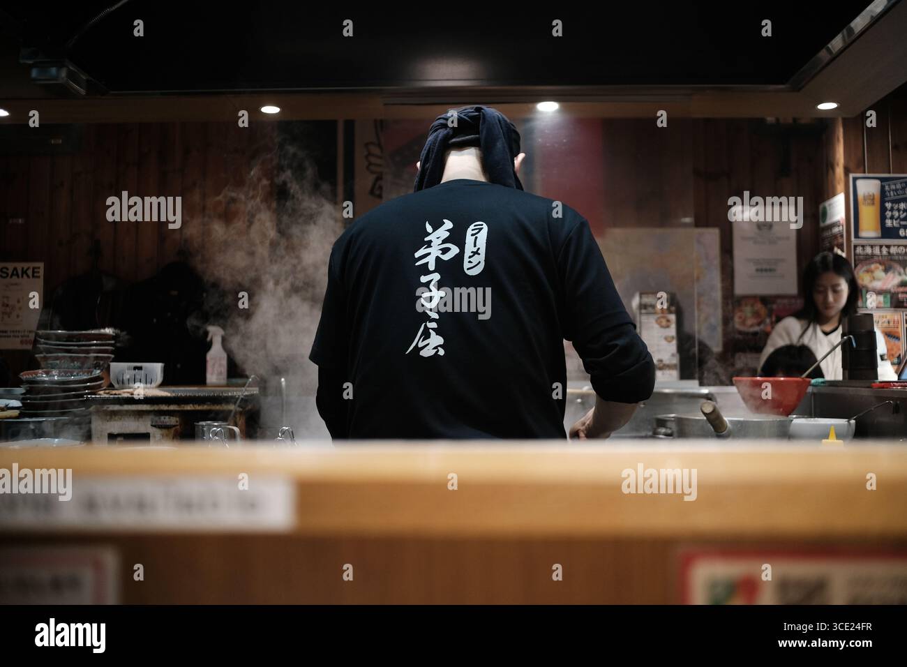 Japanischer Ramen-Koch kocht in einer traditionellen Restaurantküche mit aufsteigendem Dampf, von hinter der Theke aus gesehen Stockfoto