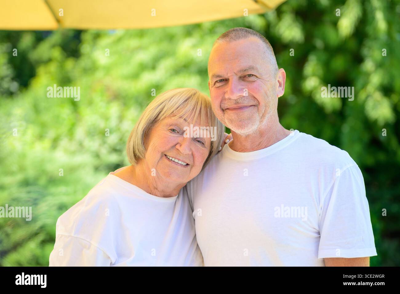 Porträt eines glücklichen Seniorenpaares, das sich in einem sonnigen grünen Garten umschließt. Stockfoto