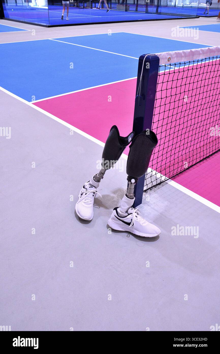 Ein Paar Beine unter dem Knie, die nebeneinander am Rand eines Pickleball-Platzes stehen, mit Netz und farbenfrohen Feldlinien. Stockfoto