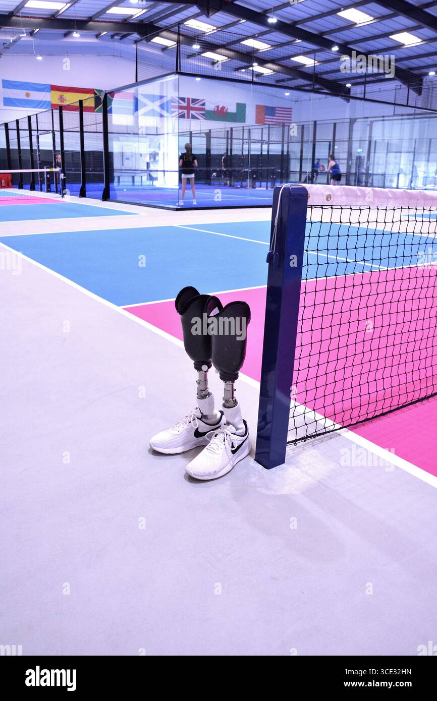 Ein Paar Beine unter dem Knie, die nebeneinander am Rand eines Pickleball-Platzes stehen, mit Netz und farbenfrohen Feldlinien. Stockfoto