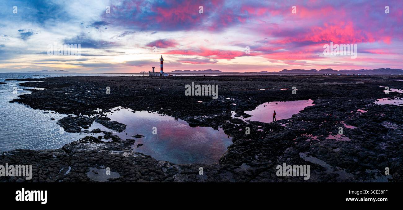 Wanderer, der den romantischen Himmel bei Sonnenaufgang über dem Leuchtturm El Toston betrachtet, aus der Luft, Fuerteventura, die Kanarischen Inseln, Spanien Stockfoto