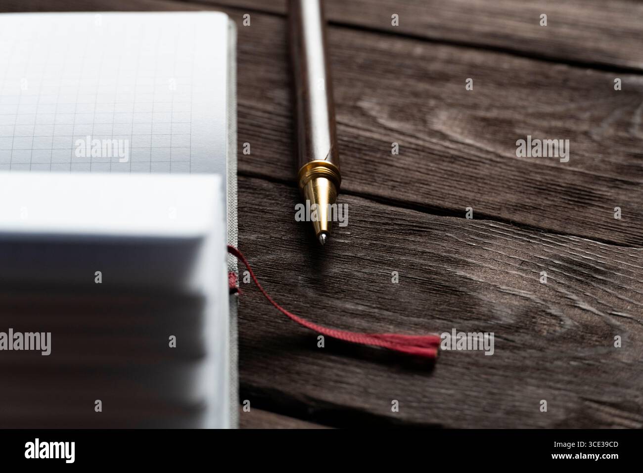 Ein Notizbuch aus Raster liegt offen auf einem rustikalen Holztisch, begleitet von einem eleganten schwarzen Stift und einem roten Lesezeichen, das die warmen Texturen von W hervorhebt Stockfoto
