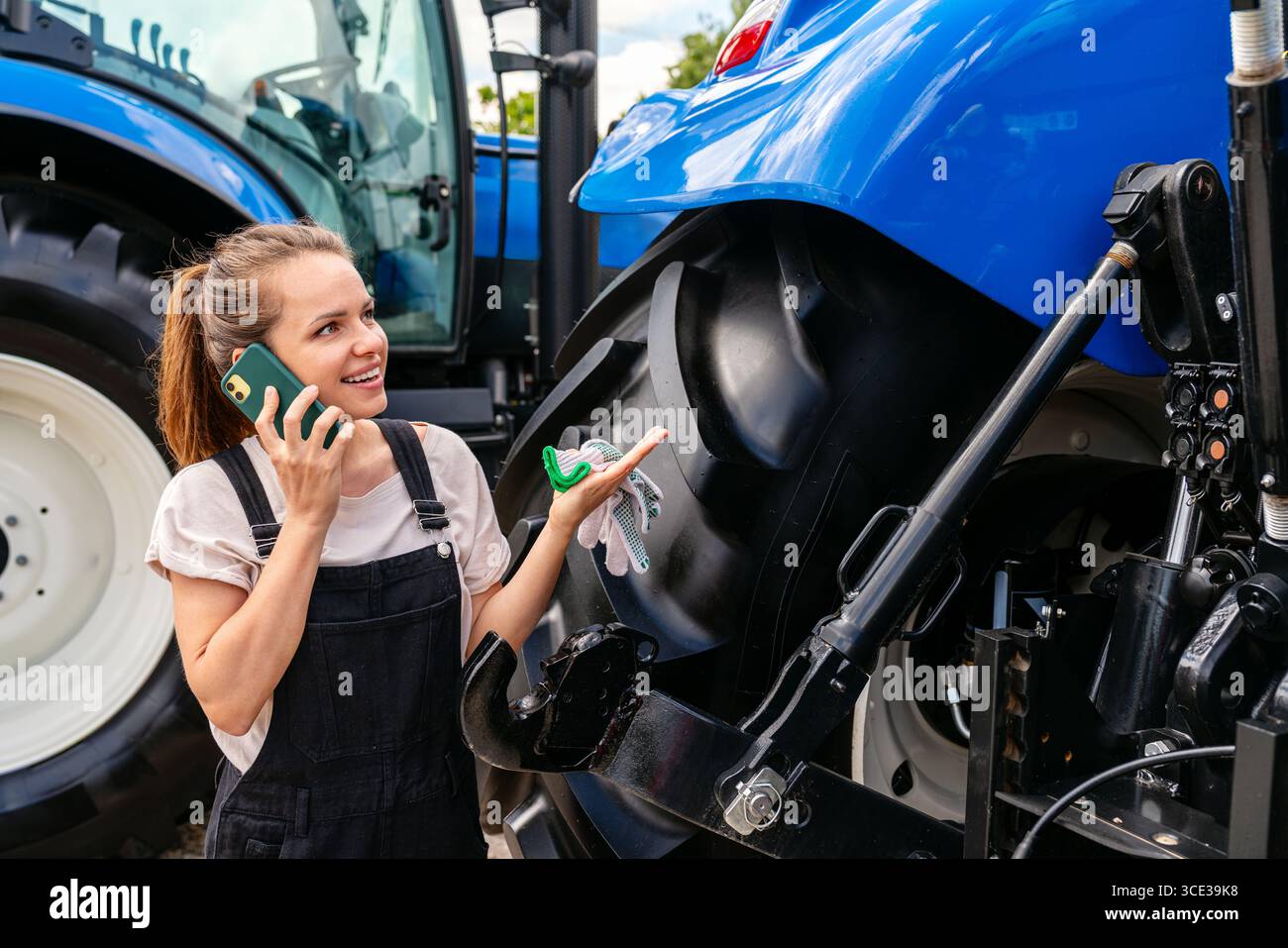 Eine Farmerin, die in der Nähe des Traktors steht und draußen auf dem Handy spricht Stockfoto