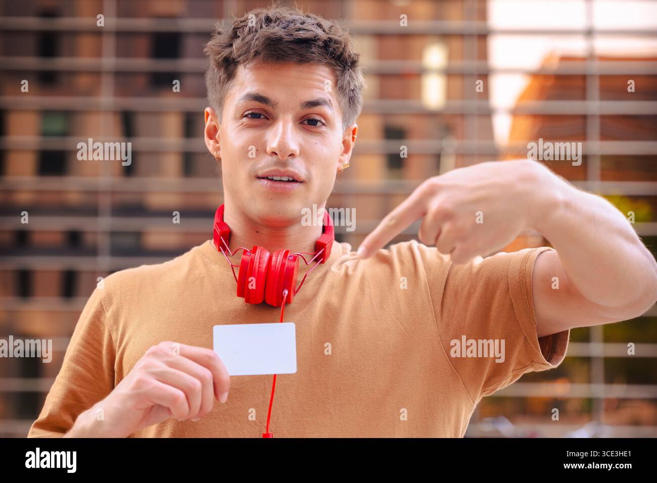 Ein lächelnder junger Mann, der auf die Kamera zeigt und draußen eine leere Visitenkarte hält Stockfoto