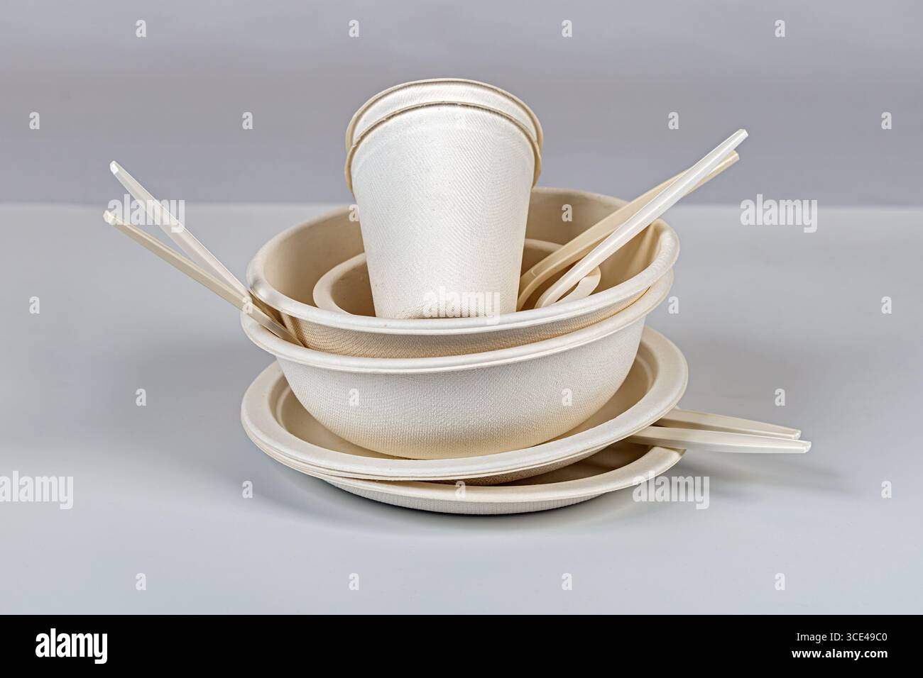 Ein stapelbarer, biologisch abbaubarer Teller, Schüsseln und Tassen mit Stäbchen auf neutralem Hintergrund mit umweltfreundlichem Einweggeschirr Stockfoto