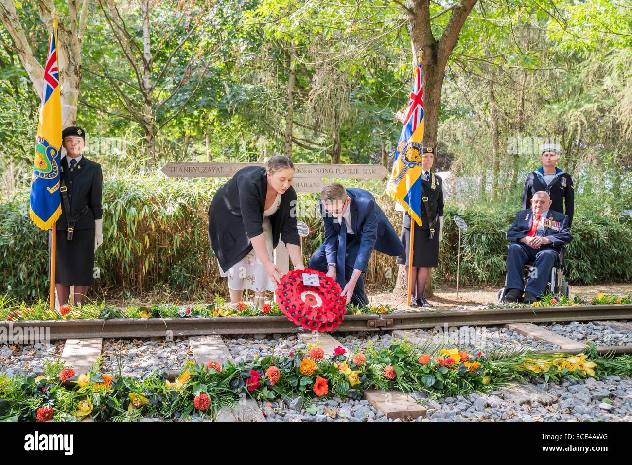 Veteran des Zweiten Weltkriegs Alfred Conway (rechts) aus Lincolnshire, der bei der Royal Navy diente, beobachtet, wie seine Urenkel Sarah-Jayne Carpenter (links) und James Carpenter (zweiter links) während eines Empfangs für VJ-Veteranen und ihre Familien im Aspect Building einen Kranz auf dem Denkmal der Burma Thailand Railway im 80 National Memorial Arboretum in Alreaffordshire legen. Bilddatum: Freitag, 15. August 2025. Stockfoto
